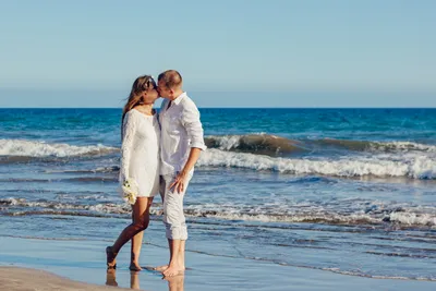 Счастливая молодая влюбленная пара на фоне моря гуляет по пляжу на фоне  голубого неба и веселится летним днем. | Премиум Фото